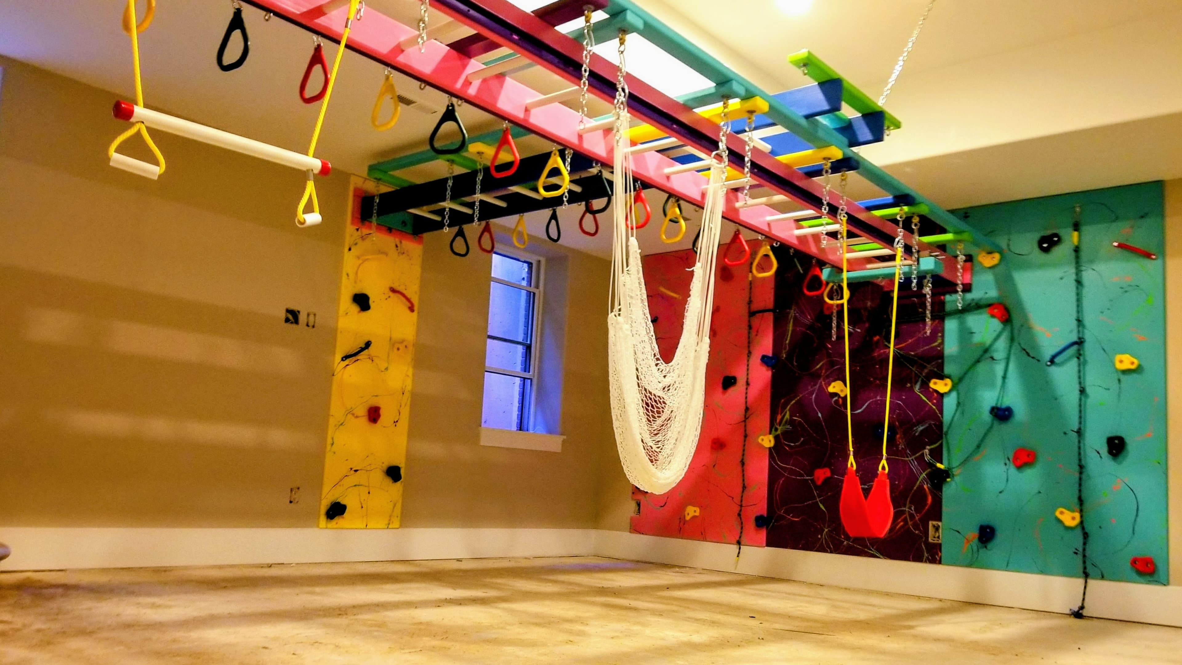 Residential basement gym with rainbow overhead beam, hammock swing, and climbing walls