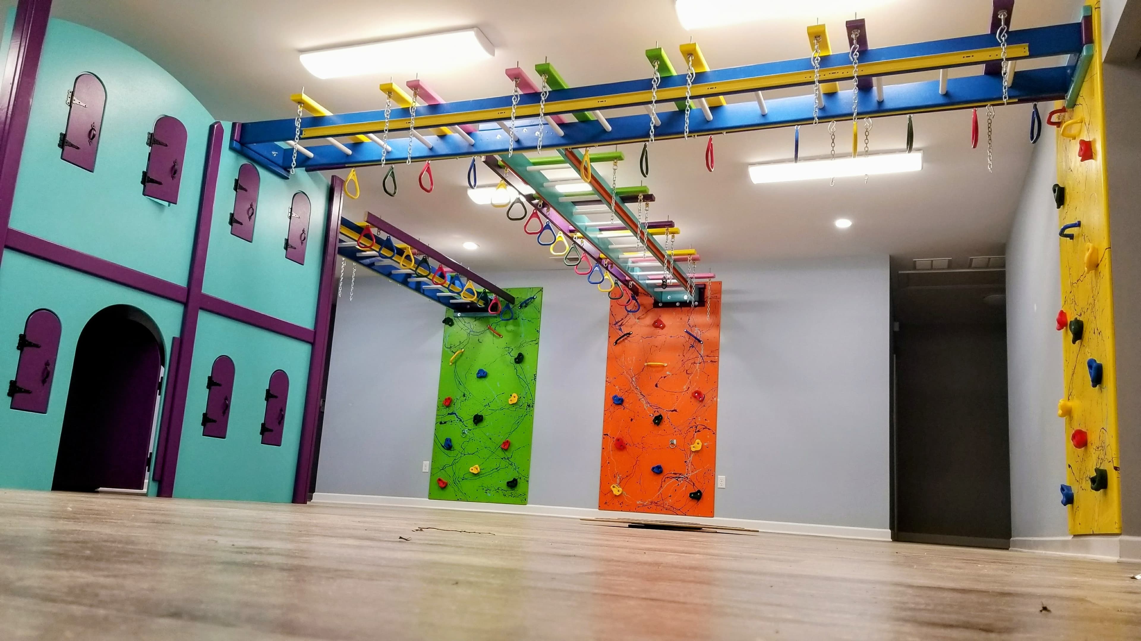 Full residential gym with ceiling-mounted overhead track, climbing walls, and colorful equipment