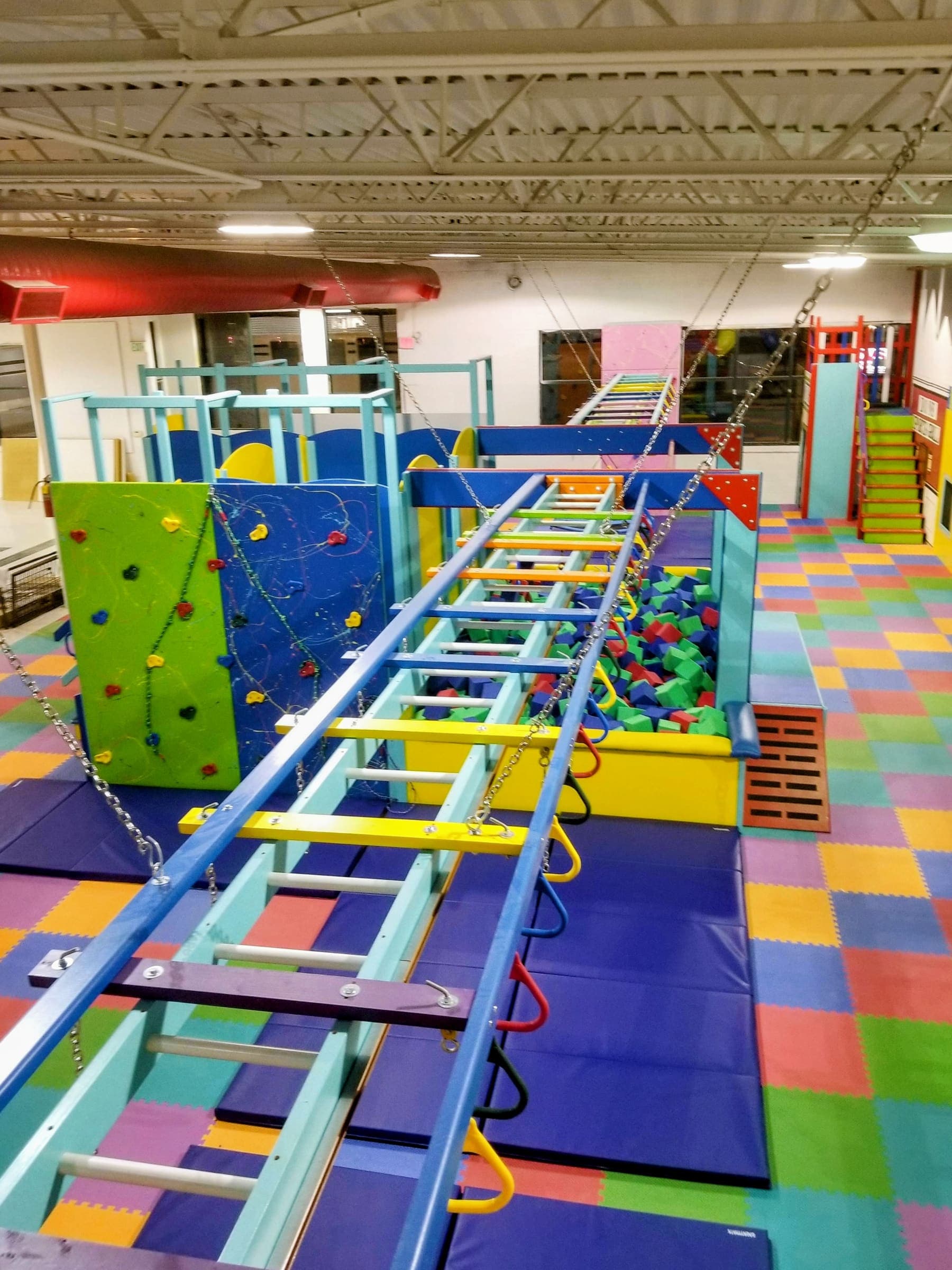 Foam cube pit beneath an overhead ladder bridge with rings and climbing walls