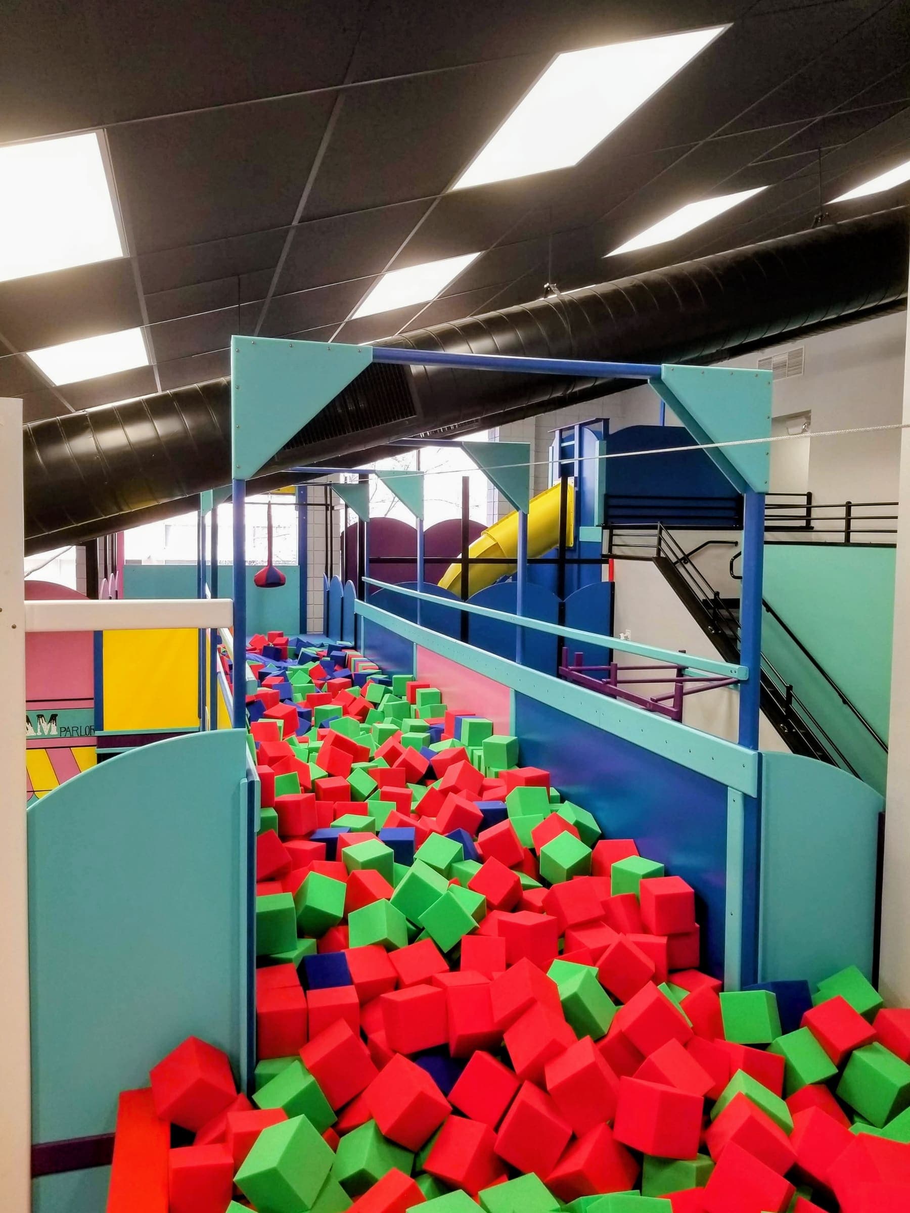 Long foam pit of red and green cubes under a zip line with a yellow tube slide behind