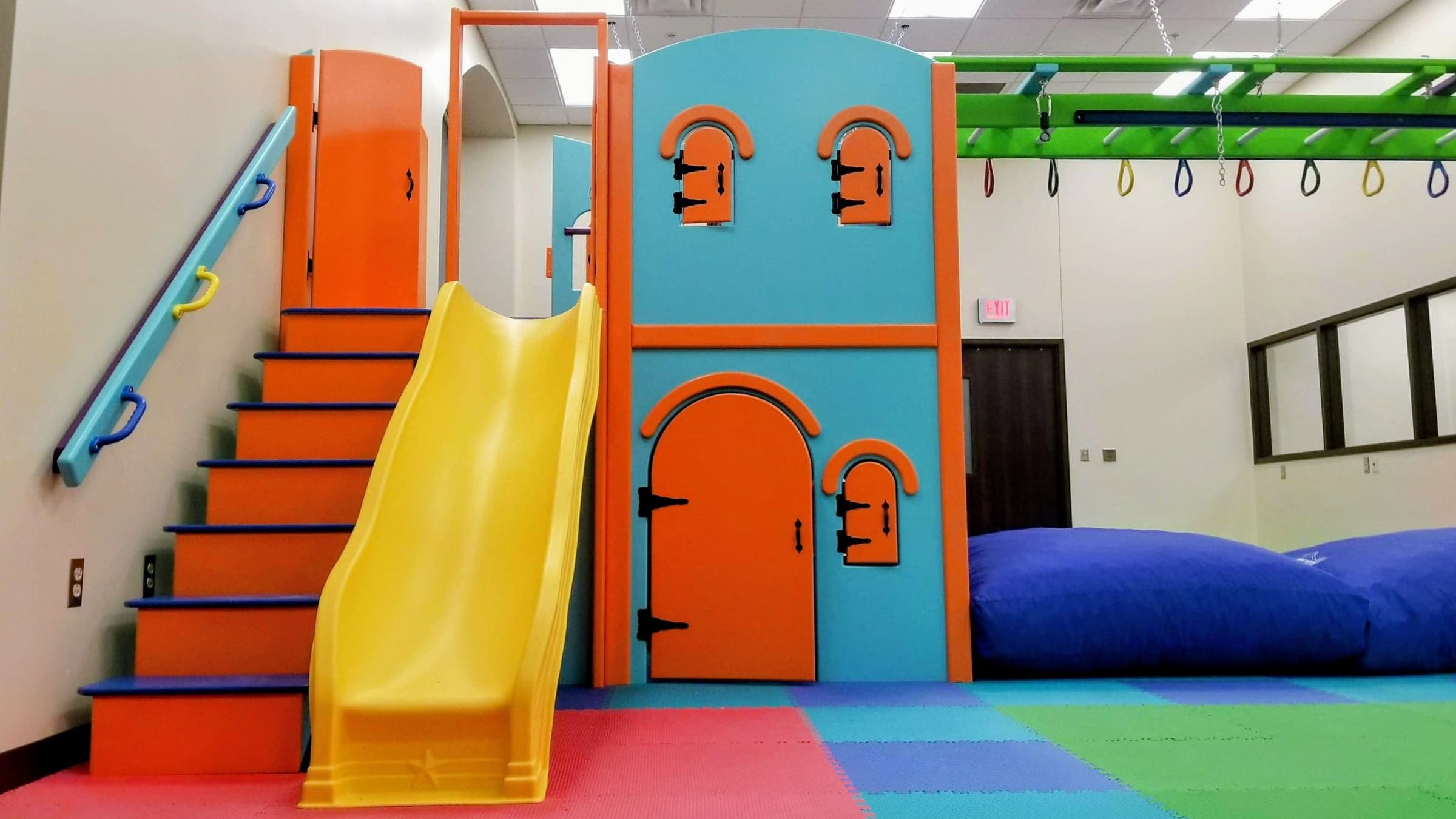 Low castle playhouse with yellow slide, padded stairs, and grab-handle rail for young climbers