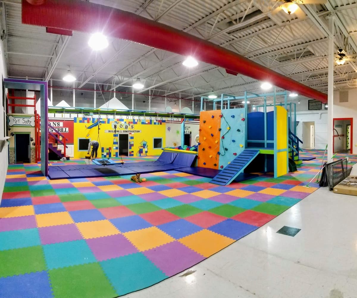 Large open sensory gym with themed murals, platform swing, climbing wall, and interlocking foam mats