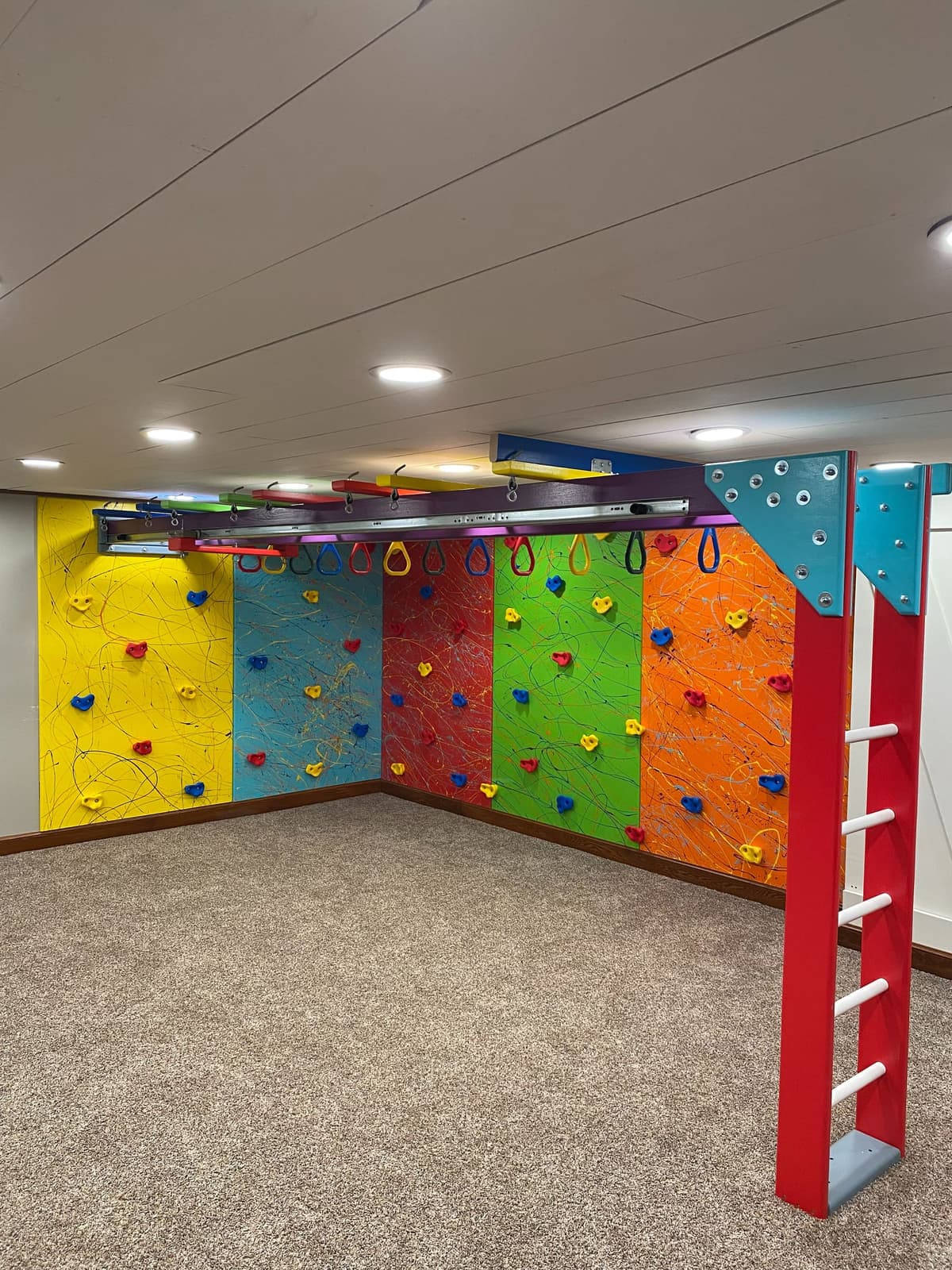 Compact basement sensory gym with five splatter climbing walls, purple ring beam, and red ladder