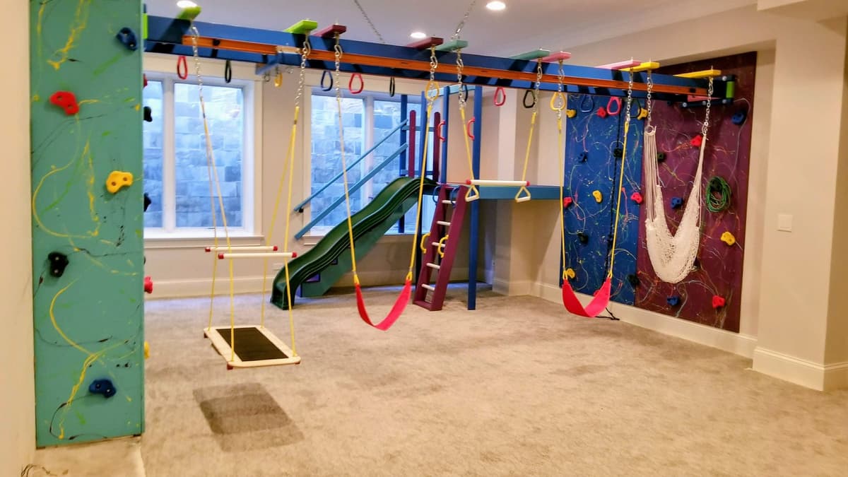 Full basement sensory gym build with climbing walls, platform swing, red swings, hammock, and green slide