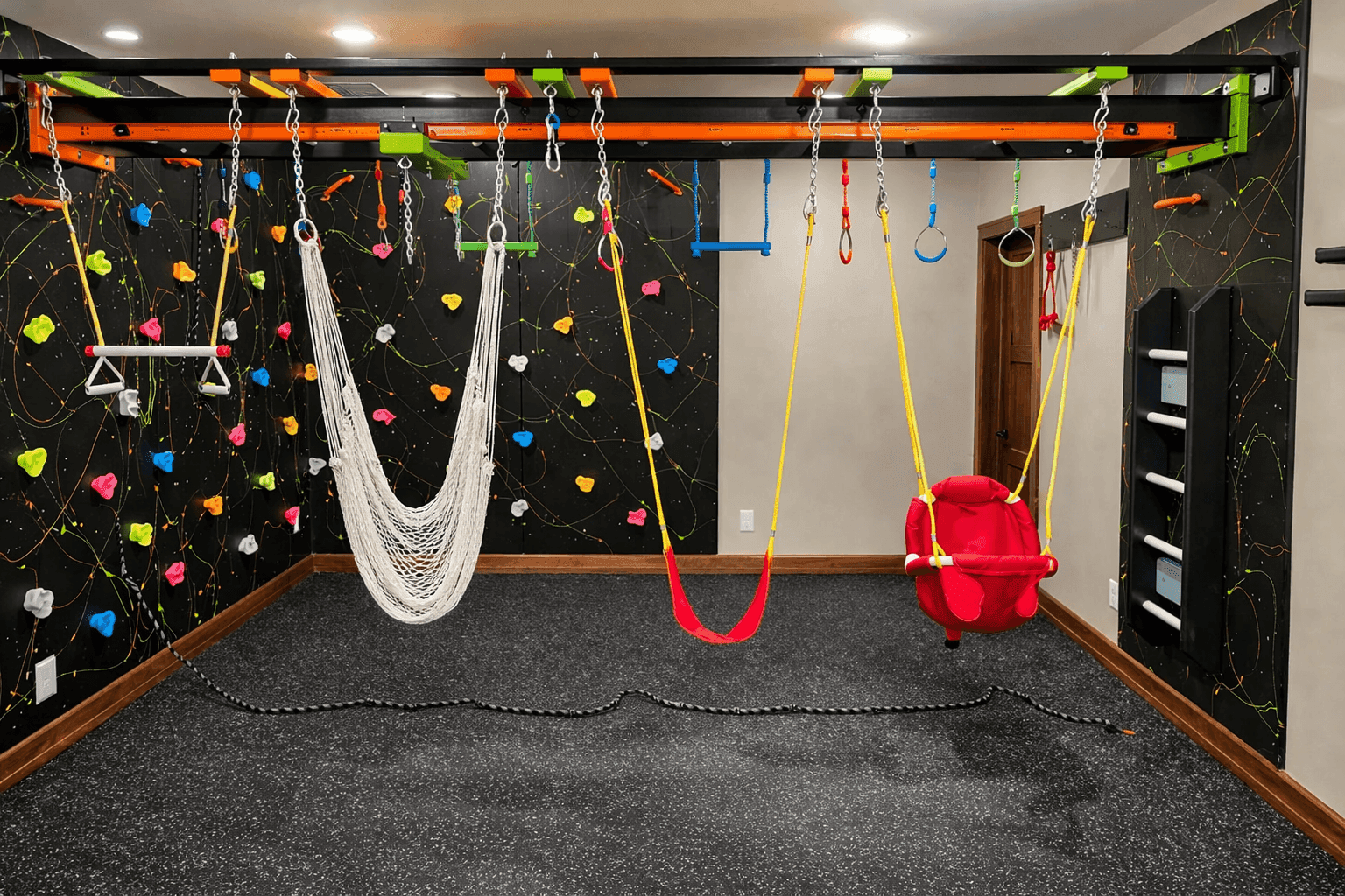 Dark themed home sensory gym with neon climbing holds, rope hammock, red swing, and bucket swing